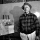 Black and white portrait of Raoul Dufy standing beside an easel displaying his botanical drawings.